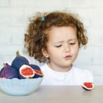 Małe nieszczęśliwe dziecko, dziewczynka patrzy na figi z niechęcią i obrzydzeniem