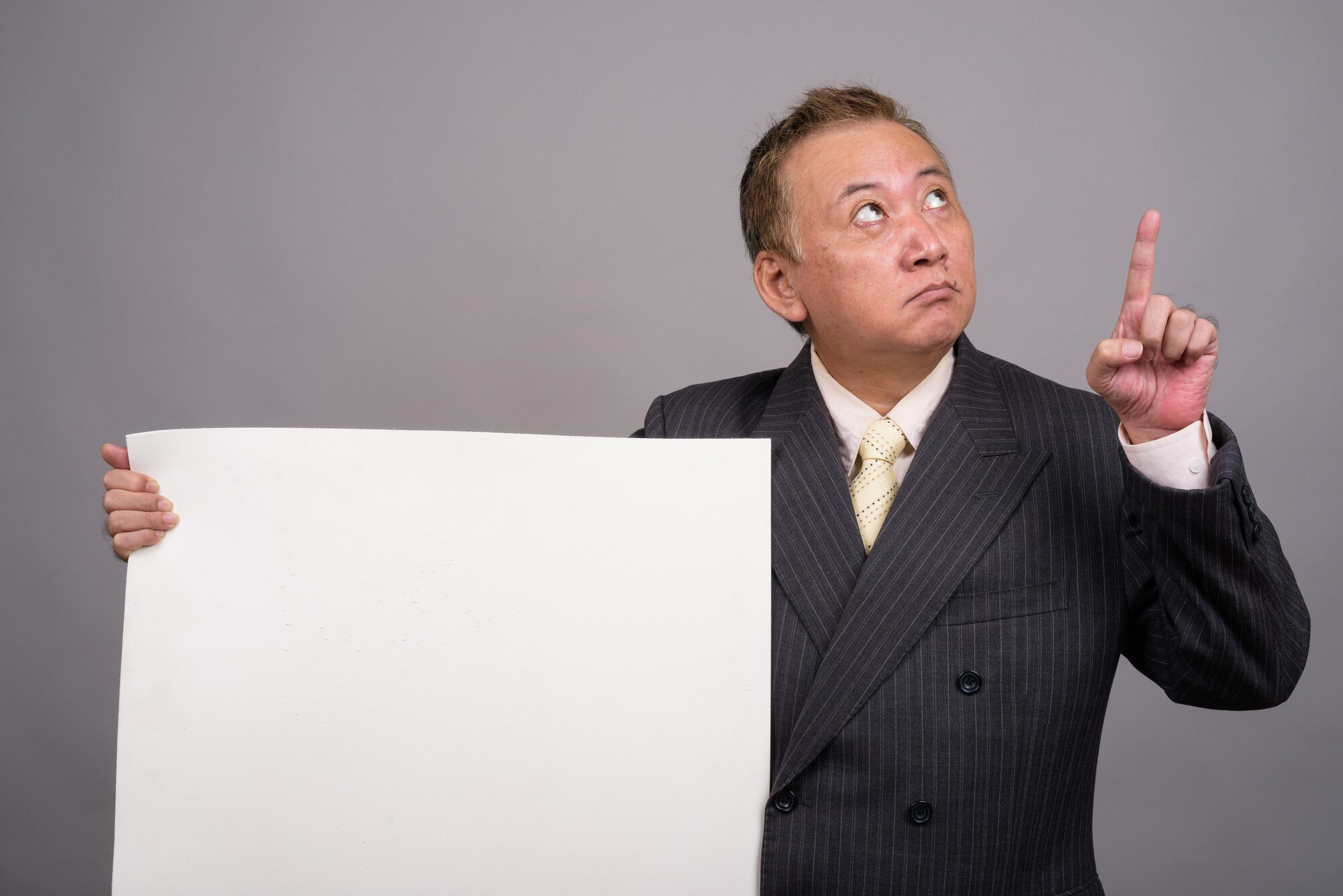 Portret dojrzałego biznesmena azjatyckich przeciw szarej ścianie