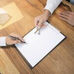 Środkowa sekcja sprzedawcy trzymającego klucze do domu przez klienta podpisującego papier na biurku