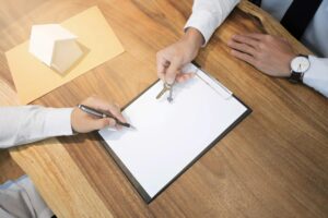 Środkowa sekcja sprzedawcy trzymającego klucze do domu przez klienta podpisującego papier na biurku