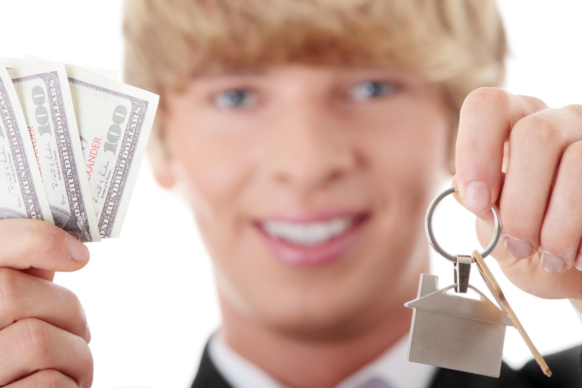 Portret uśmiechniętego biznesmena trzymającego papierową walutę i klucz do domu na białym tle