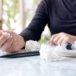 Środkowa sekcja kobiety trzymającej zmarszczone papiery podczas siedzenia z książkami na stole