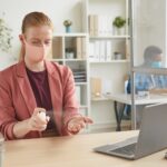 Portret młodej bizneswoman noszenie maski odkażania rąk podczas pracy przy biurku w szafie w biurze po pandemii