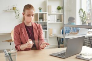 Portret młodej bizneswoman noszenie maski odkażania rąk podczas pracy przy biurku w szafie w biurze po pandemii