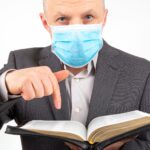Mężczyzna w garniturze z maską medyczną na twarzy studiuje Biblię.