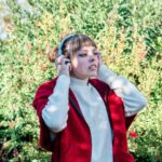 Młoda dziewczyna kaukaski w czerwonej kurtce, która słucha muzyki w niebieskich słuchawkach w parku