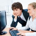 Uśmiechnięci i młodzi biznesmeni pracujący razem nad komputerem