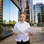 Biznesowa kobieta sukcesu z dokumentami w ręku na tle centrum biurowego