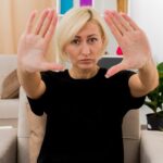 Przekonana, piękna blondynka Rosjanka siedzi na fotelu, wyciągając ręce, patrząc na kamery w salonie