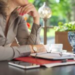 Przerwa na kawę, stół w restauracji na świeżym powietrzu, dokumenty biznesowe, notebook, smartfon, okulary, filiżanka kawy. Odpoczywająca kobieta biznesu