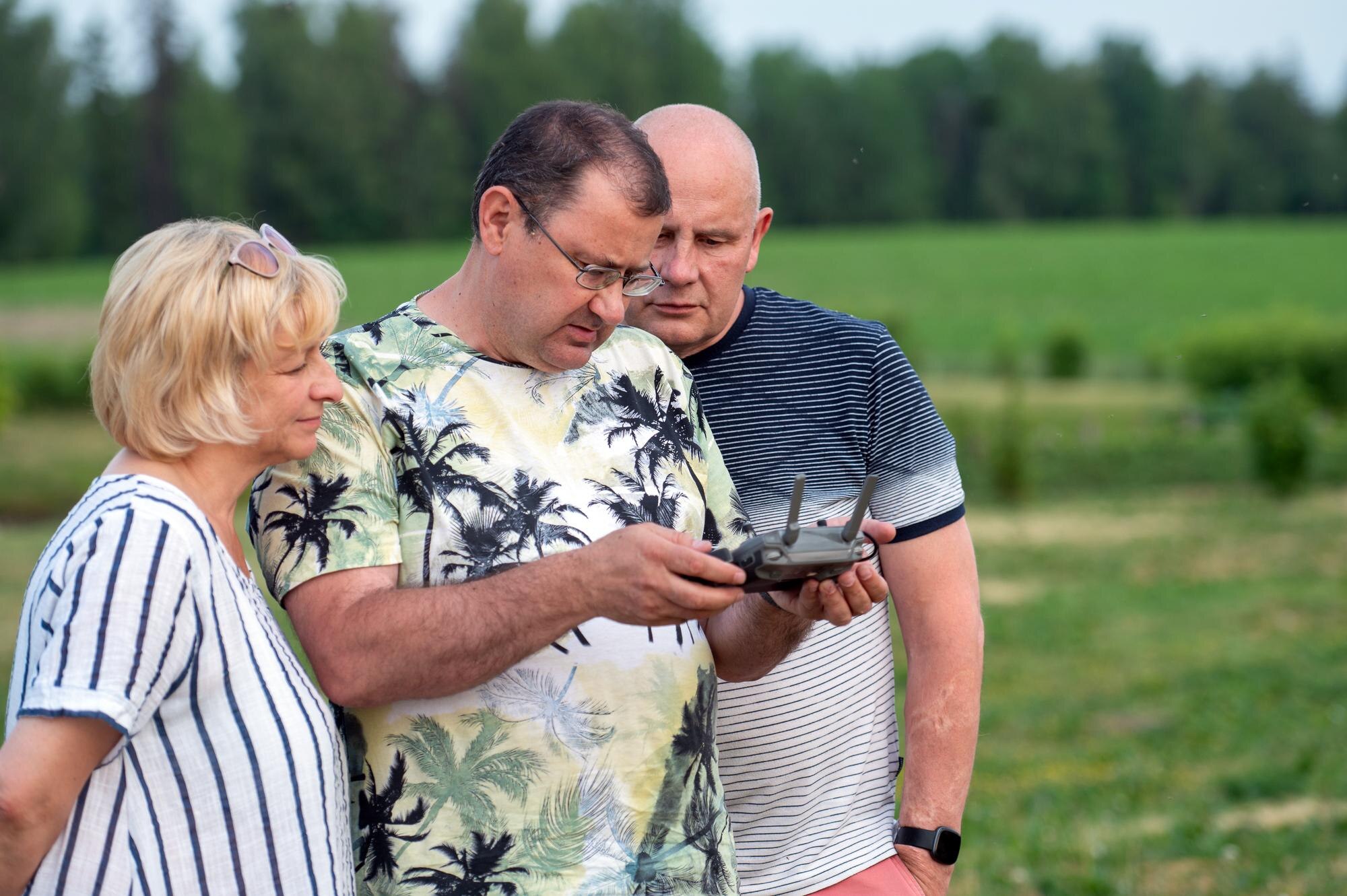 Grupa dojrzałych ludzi oglądających ekran zdalnego sterowania dronem w parku