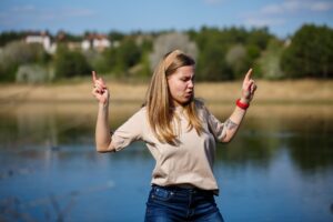 Dziewczyna tańczy w pobliżu jeziora, słoneczna pogoda. Młoda kobieta raduje się życiem, tańczy i śpiewa. Ma dobry nastrój i uśmiech na twarzy.