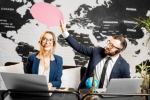 Para travel managerów marząca z kolorowymi bąbelkami nad głową siedząca w biurze agencji na tle mapy świata