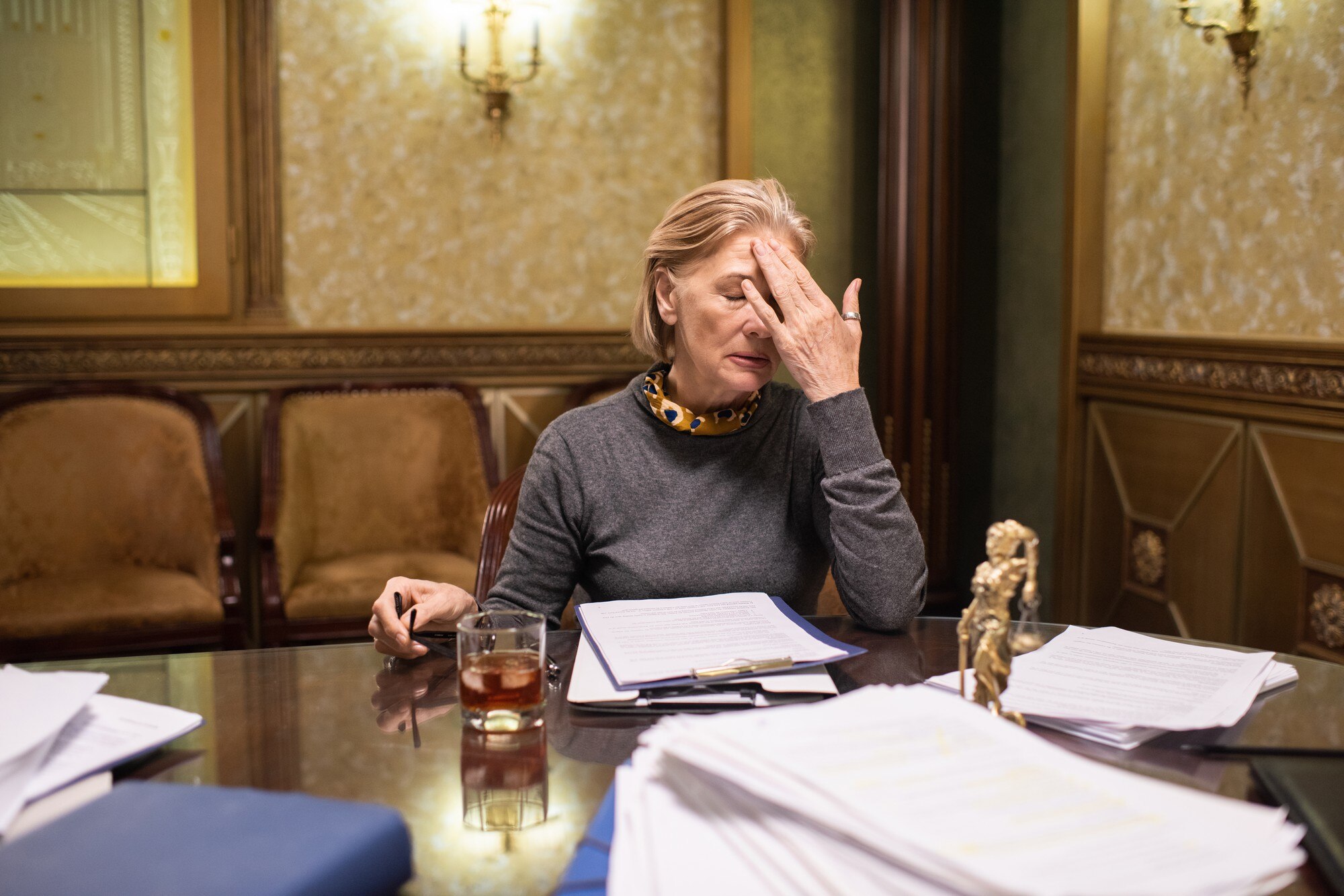 Blond dojrzała prawniczka dotyka głowy podczas pracy w godzinach nadliczbowych