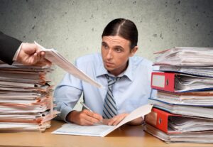 Młody przepracowany kierownik w miejscu pracy ze stosami dokumentów