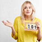 Zdziwiona atrakcyjna kobieta w żółtych ubraniach z kalendarzem myśli o przygotowaniu się do wakacyjnego wyjazdu, niewiele czasu zostało do pierwszego dnia lata