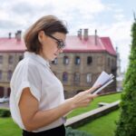 Portret nauczyciela dojrzałej bizneswoman, menedżera z dokumentami dokumentów biznesowych w ręce. Budynek szkoły, tło budynku biurowego, profesjonalna pewna siebie kobieta w okularach biała koszula