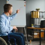 Niepełnosprawny biznesmen siedzi na wózku inwalidzkim i używa komputer W biurze