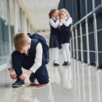 Chłopiec siedzi na podłodze Dzieci w szkole w mundurach razem na korytarzu