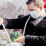 Zamaskowany mężczyzna na lokalnym targu kupuje kapustę brokułową w okresie pandemii Covid Koncepcja zakupów pandemicznych Zdjęcie wysokiej jakości