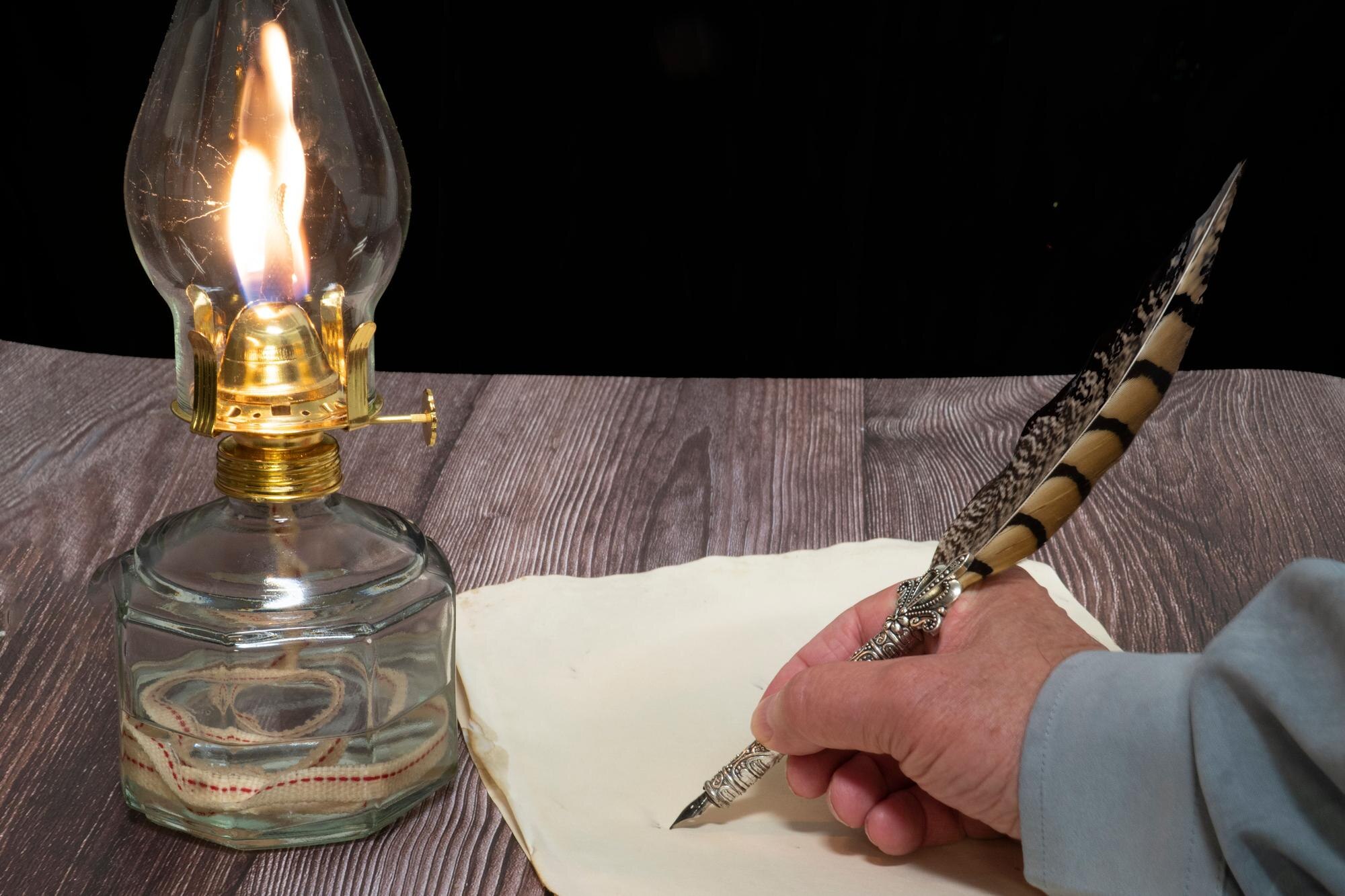 Zbliżenie lampy olejowej i osoby piszącej piórem na papierze
