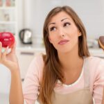 Piękna młoda kobieta w kuchni decyzja między jabłkiem lub słodkim ciastem czekoladowym.