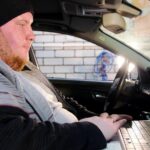 Serwis samochodowy gruby mechanik siedzi w samochodzie i pracuje z laptopem