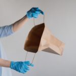 Kobieta w masce medycznej zagląda do pustej papierowej torby na białym tle Kobieta w niebieskim lateksie gl