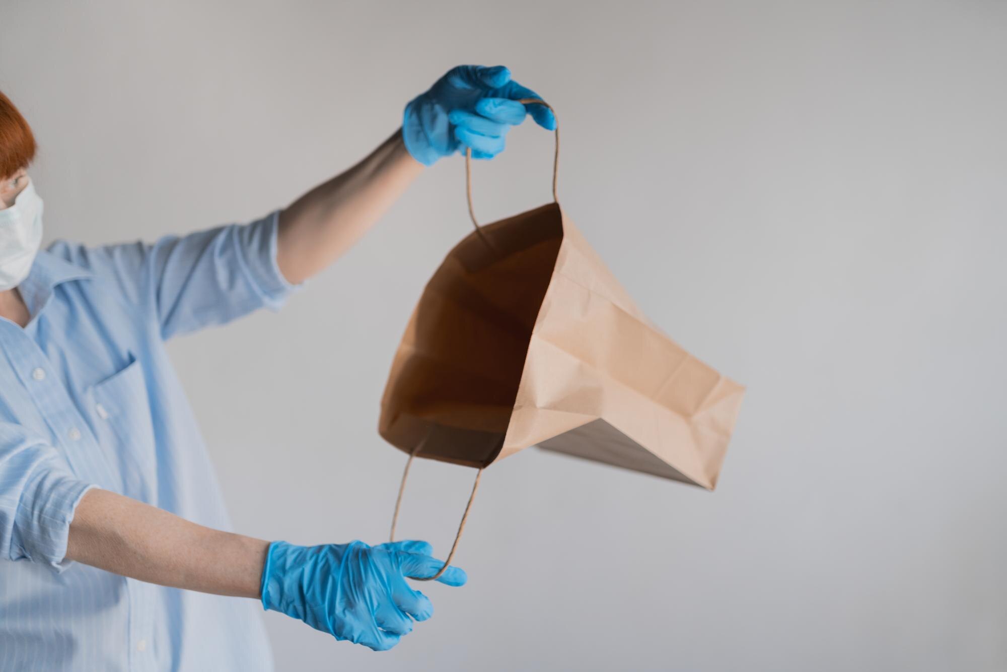 Kobieta w masce medycznej zagląda do pustej papierowej torby na białym tle Kobieta w niebieskim lateksie gl