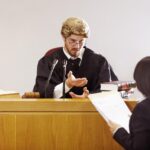 Przedstaw swoją sprawę Poważny młody sędzia siedzący na sali sądowej z surowym wyrazem twarzy