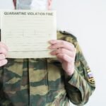 Policjant z kajdankami w mundurze w kolorze khaki zatrzymuje ludzi na ulicy za naruszenie zasad kwarantanny samoizolacji domowej z powodu pandemii grypy covid19 koronowirusaŻółty mandat