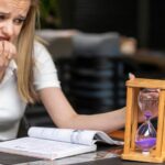 Nerwowa pani trzymająca klepsydrę i obgryzająca paznokcie