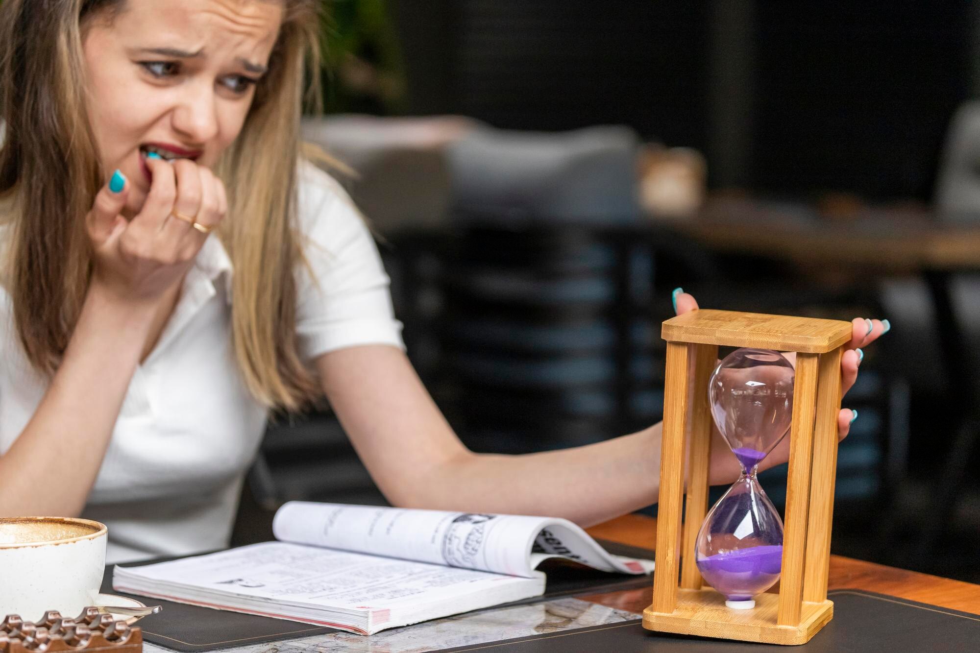 Nerwowa pani trzymająca klepsydrę i obgryzająca paznokcie