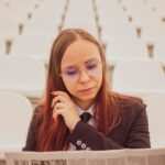 Kobieta w okularach i garniturze czyta gazetę siedząc na stadionie