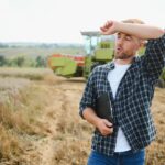 Szczęśliwy rolnik dumnie stojący na polu Kierowca kombajnu zamierza skosić bogate zbiory pszenicy Agronom w flanelowej koszuli patrzący na kamerę na polu uprawnym