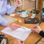 Klient podpisuje dokument dotyczący działalności na rynku nieruchomości obok prawnika lub pośrednika w obrocie nieruchomościami siedząc przy biurku Koncepcja biznesowa sprzedaży i kupna domuKoncepcja wynajmu nowego domu