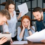 Portret zmęczonej kobiety biznesu siedzącej przy stole wieloetnicznych kolegów potrząsających dokumentami