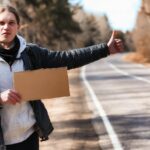 Młody mężczyzna podróżuje autostopem po kraju Mężczyzna próbuje złapać przejeżdżający samochód na podróż Mężczyzna z plecakiem pojechał autostopem na południe