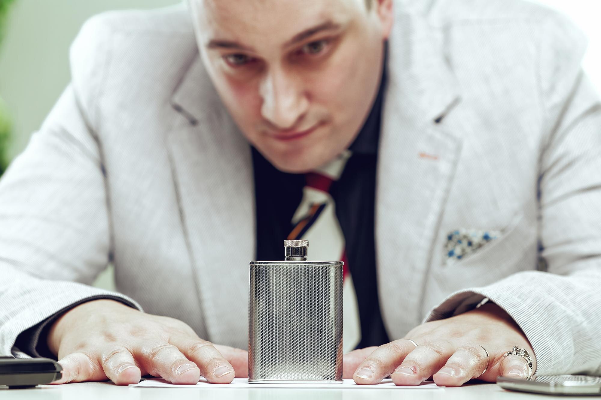 Biznesmen siedzi przy swoim biurku i intensywnie wpatruje się w kolbę umieszczoną przed nim.