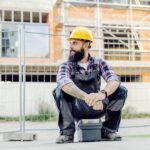 Pracownik siedzący na skrzynce narzędziowej i czekający na przejażdżkę na placu budowy