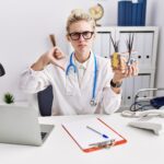 Młoda kobieta lekarz trzymająca model ludzkiej anatomicznej skóry i włosów w klinice z negatywnym znakiem wściekłej twarzy pokazującym niechęć z koncepcją odrzucenia kciuków w dół