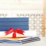 Dyplom ukończenia studiów z książkami i zeszytami na stole na niewyraźnym tle