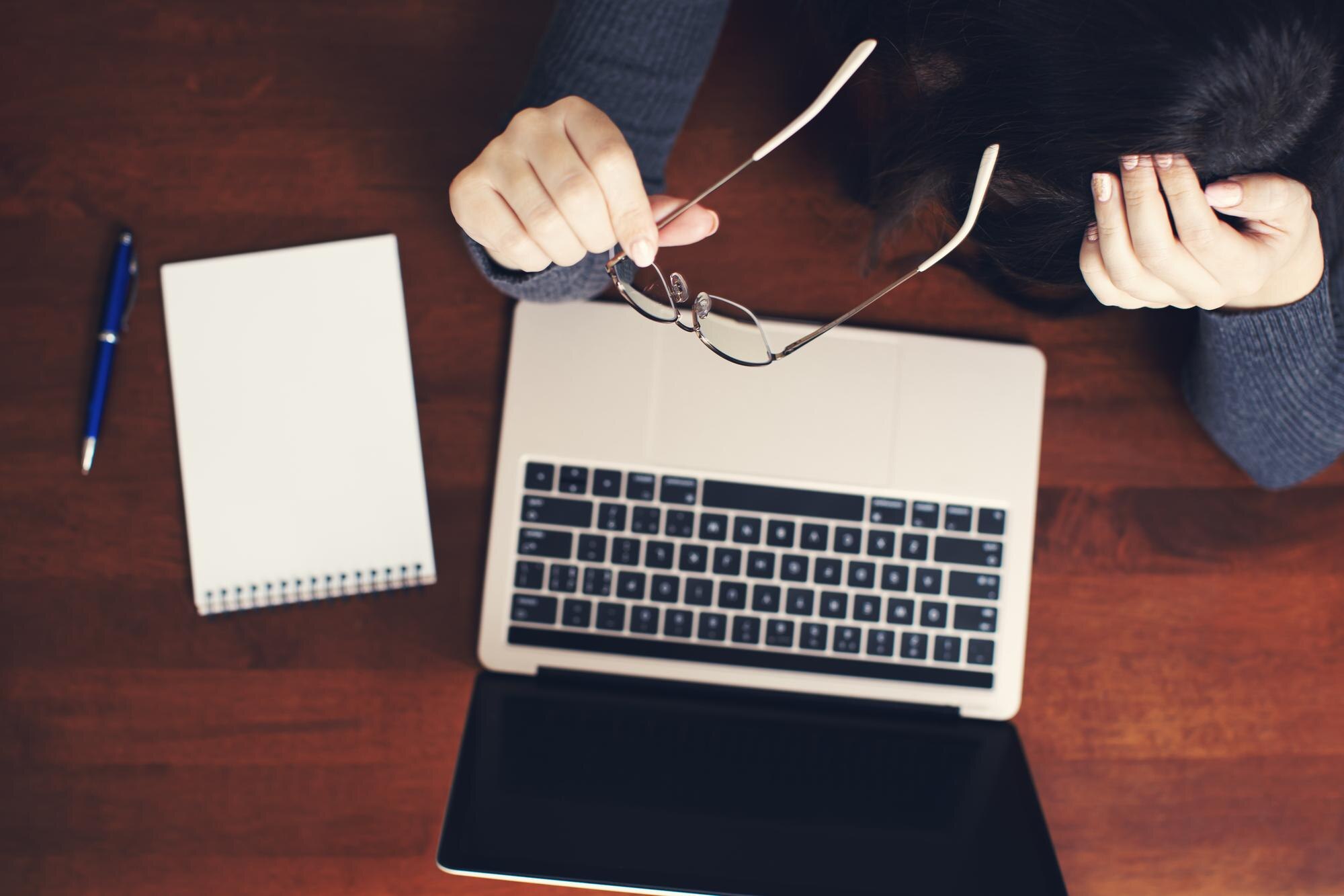 Widok z góry bizneswoman trzymając okulary podczas pracy na laptopie przy biurku