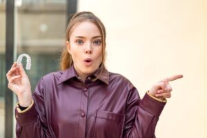 Młoda ładna dziewczyna trzyma niewidzialne szelki na zewnątrz zaskoczona i wskazująca stronę