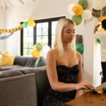 Young woman preparing decorations while friends hang birthday banner in living room