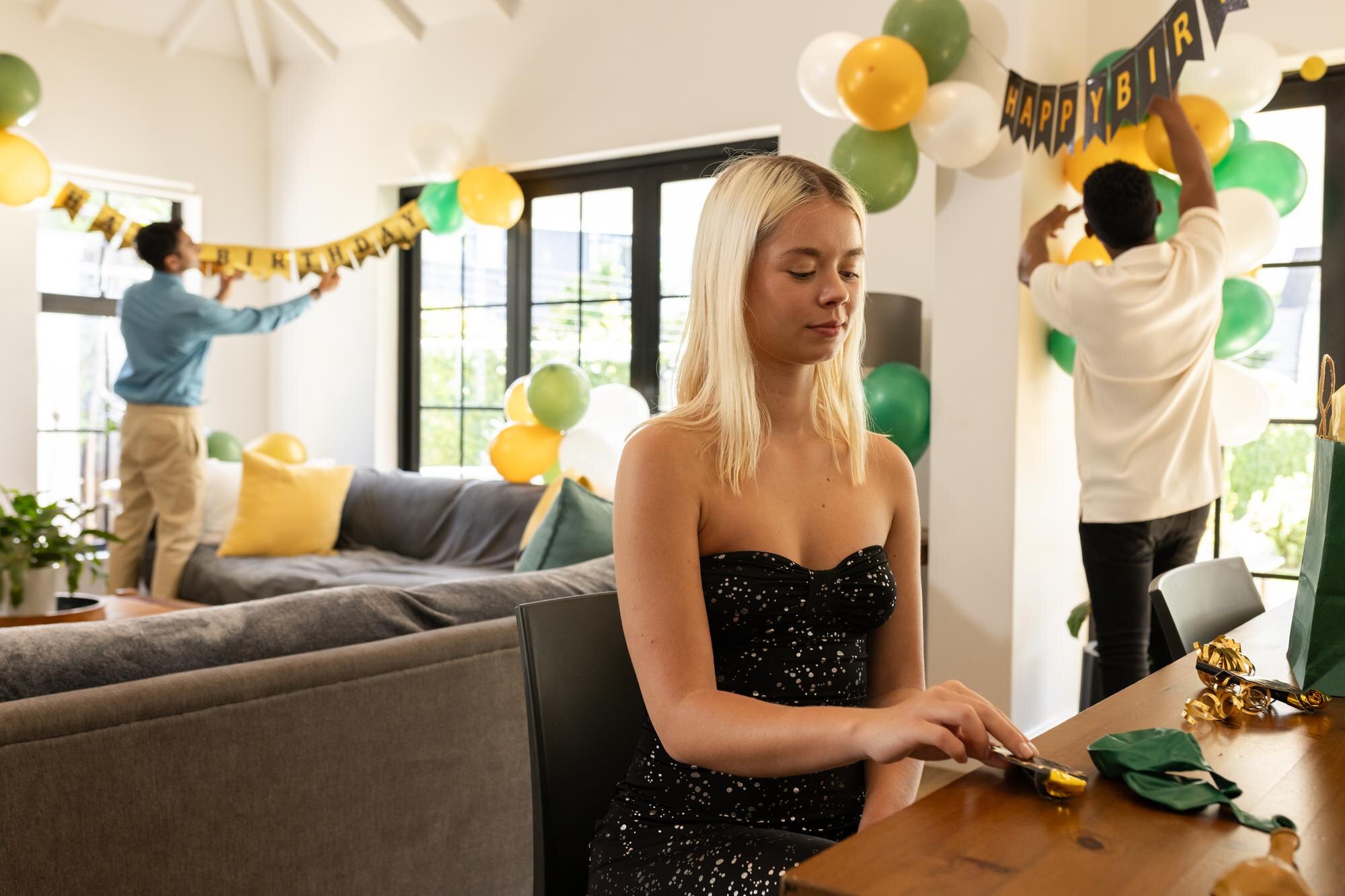 Young woman preparing decorations while friends hang birthday banner in living room
