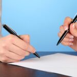 Dwóch partnerów biznesowych podpisujących dokument na niebieskim tle