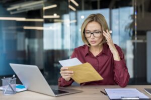 Stressed woman at a modern office desk reads an envelope with bad newsrejection notice or