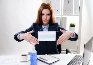 kobieta biznesu przy biurku z komputerem trzyma w dłoniach medyczną maskę