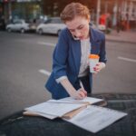 Zajęta kobieta się spieszy, nie ma czasu, będzie rozmawiać przez telefon w drodze. Bizneswoman robi wiele zadaniom Na masce samochodu. Wielozadaniowość przedsiębiorca.